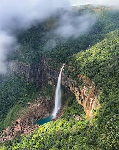 Most Beautiful Waterfalls in India featuring a majestic waterfall cascading into a turquoise pool surrounded by lush green hills and misty clouds.